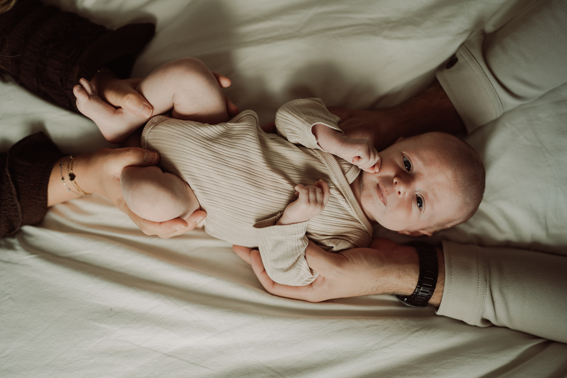 Pasgeboren baby tussen de armen van zijn ouders tijdens een newbornreportage thuis