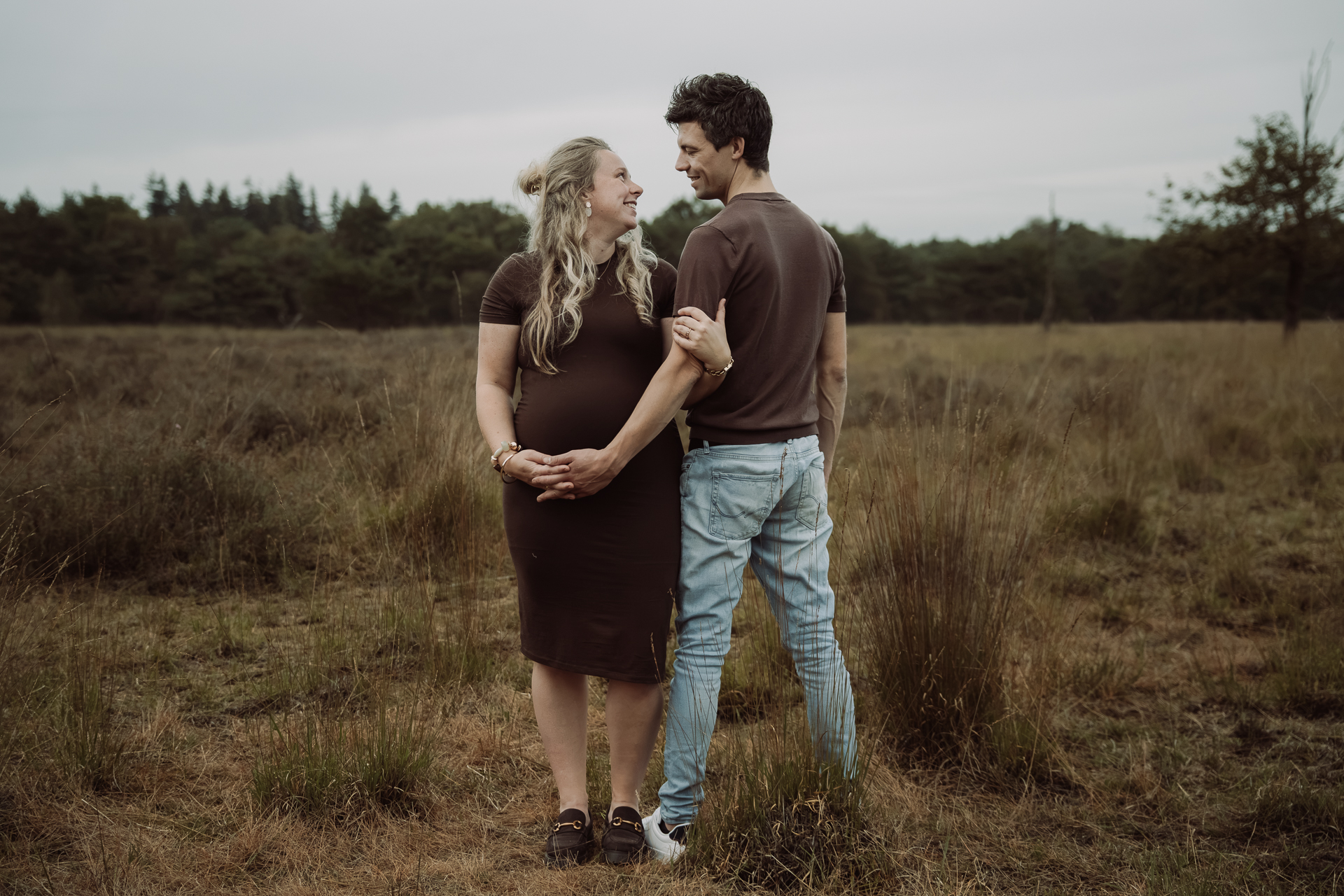 Zwangere vrouw en haar partner lachen naar elkaar terwijl ze samen hun handen onder haar buik houden